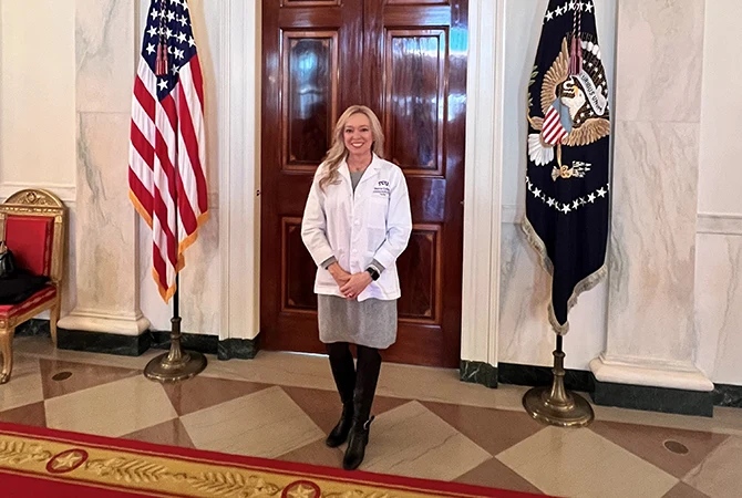 Vicki Brooks, in white medical coat, stands between two flags at the White House